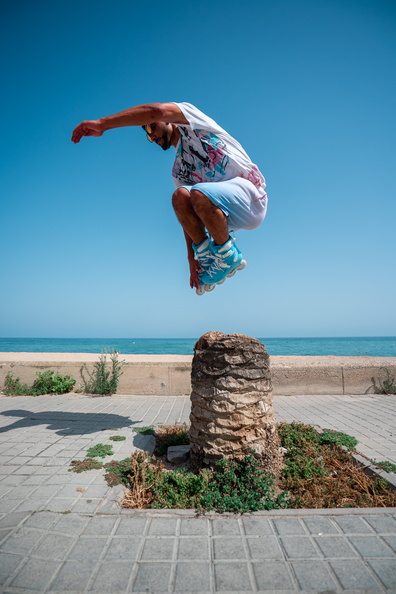 muž skákající na kolečkových inline freeskate bruslích přes palmu, brusle jsou Powerslide Storm